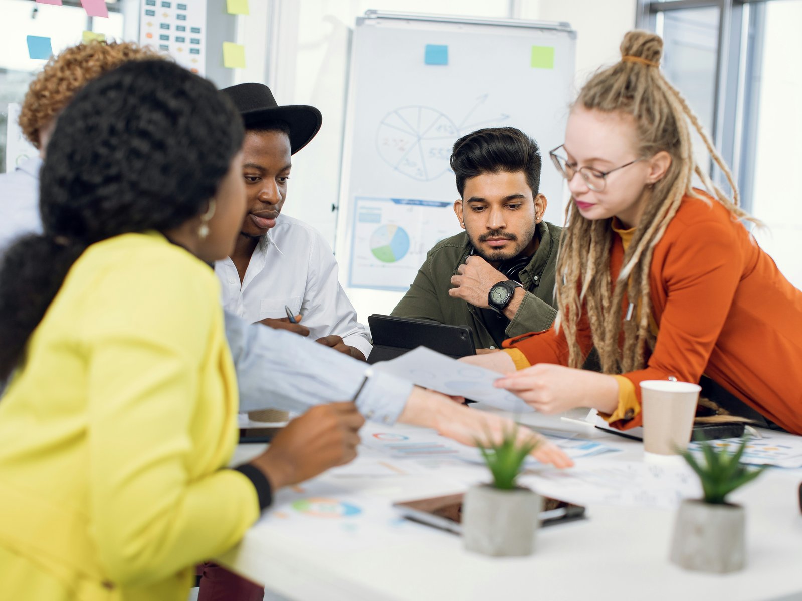 Four colleagues around a conference table reviewing printed charts and papers together, illustrating checking whether leadership practices actually exist
