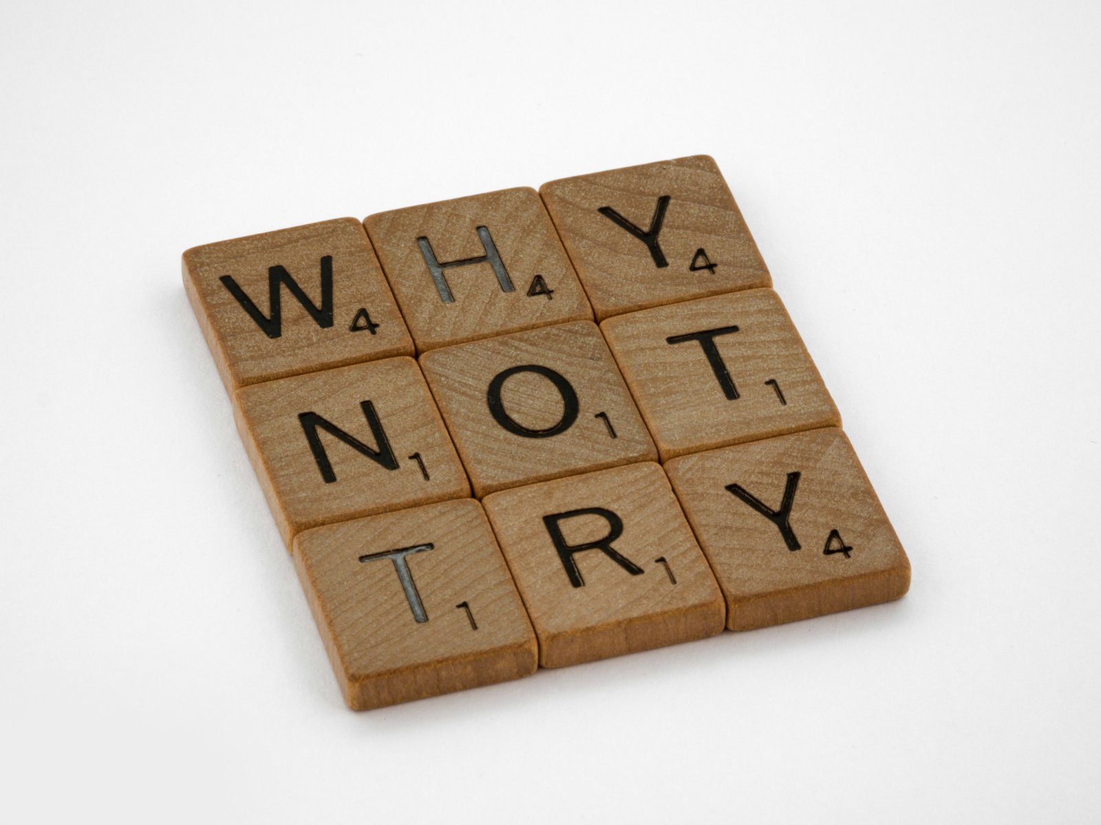 Wooden letter tiles spelling out "why not try" on a white table, a nudge for business owners to build an identity and interests beyond the business before they retire