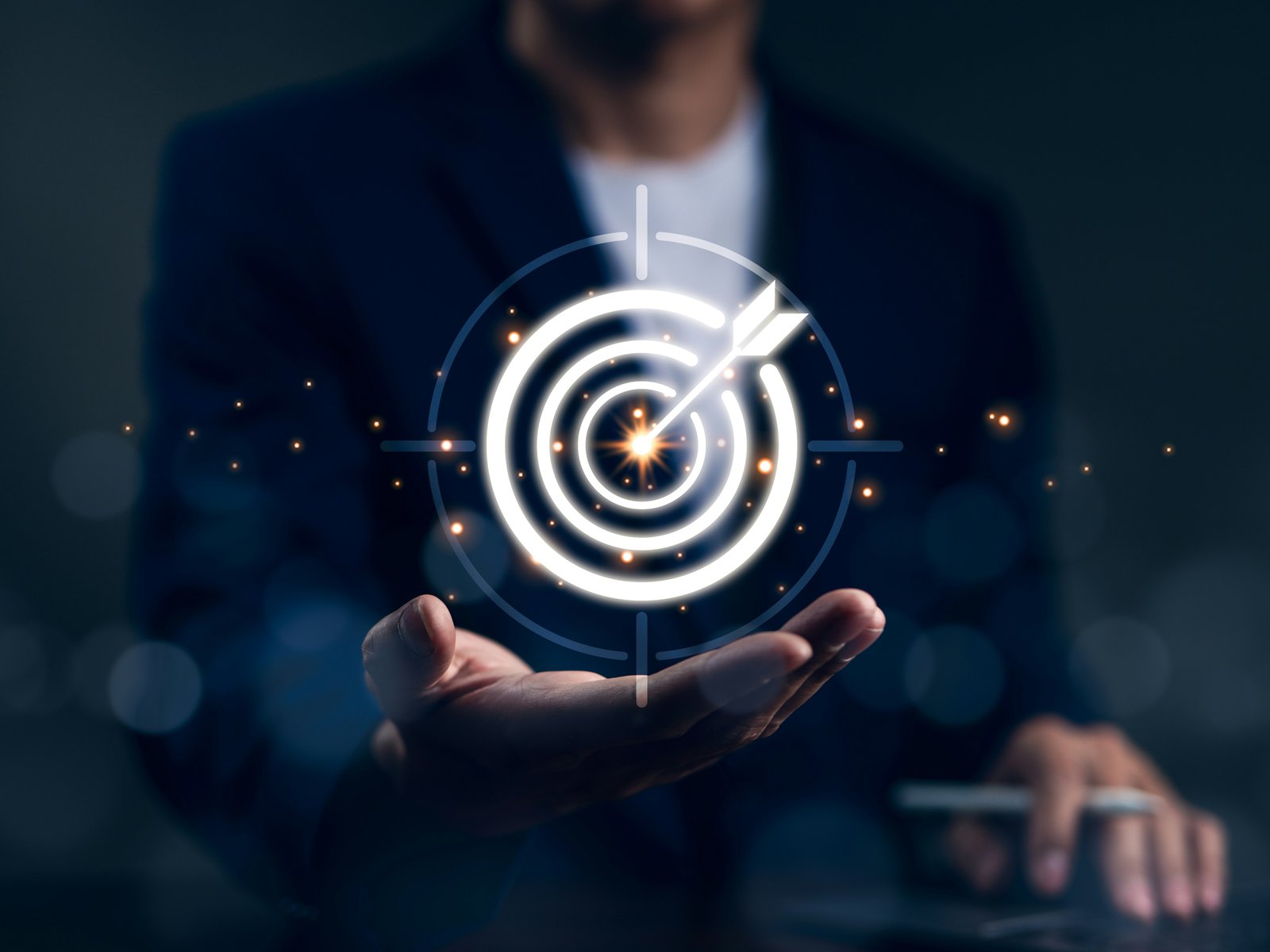 A businessman's open hand holding a glowing target with an arrow in the bullseye, a picture of what clear expectations at work give even a top performer to aim at