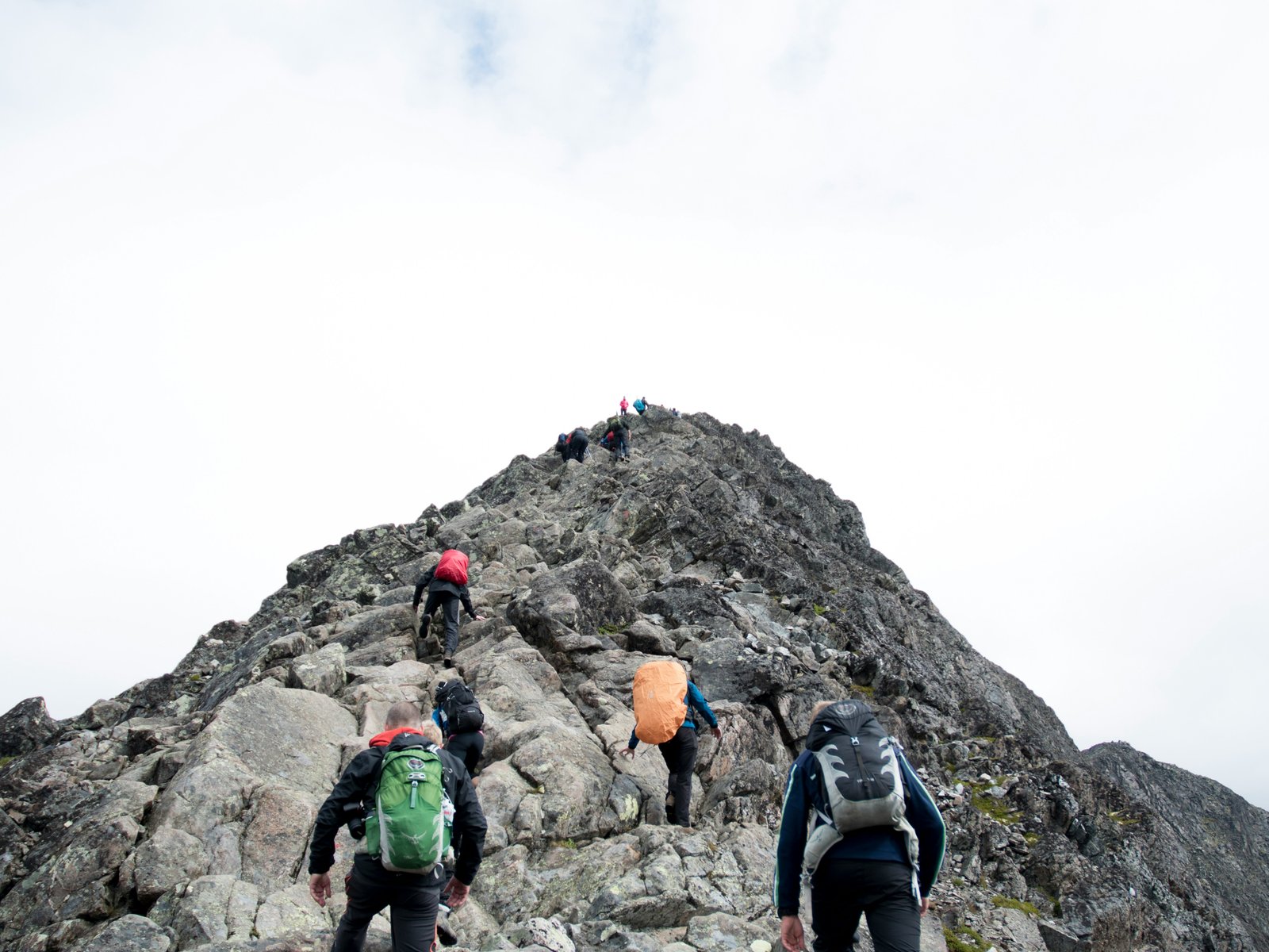 A line of hikers helping each other climb a steep, rocky mountain ridge together, the kind of shared effort it takes to coach a struggling employee up rather than writing them off