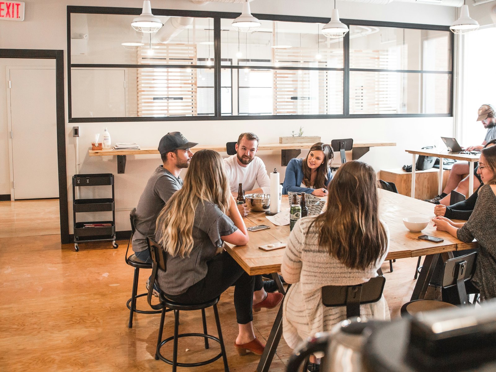 A group of coworkers gathered closely around a wooden table sharing drinks and conversation, the kind of internal warmth Unreasonable Hospitality argues has to exist before it can reach a customer