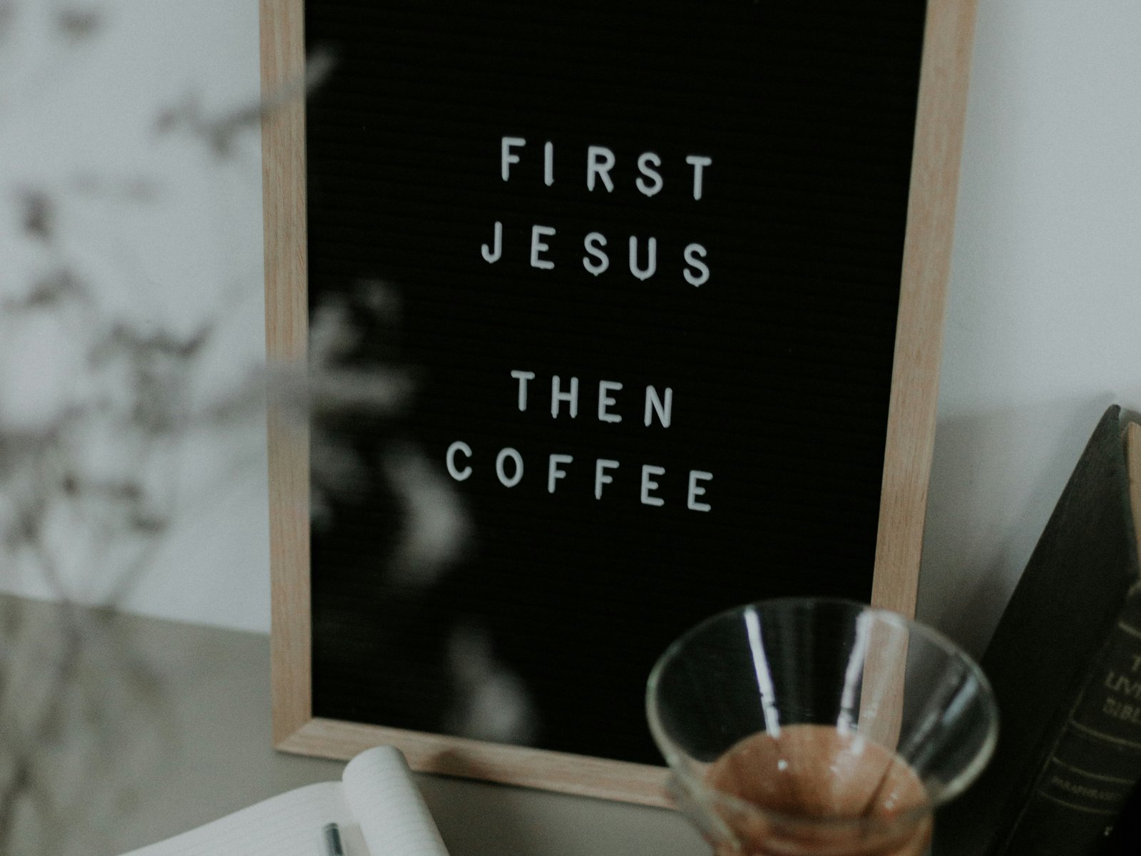 Letter board reading “First Jesus, then coffee” beside a notebook, reading glasses, and a pour-over coffee maker on a desk