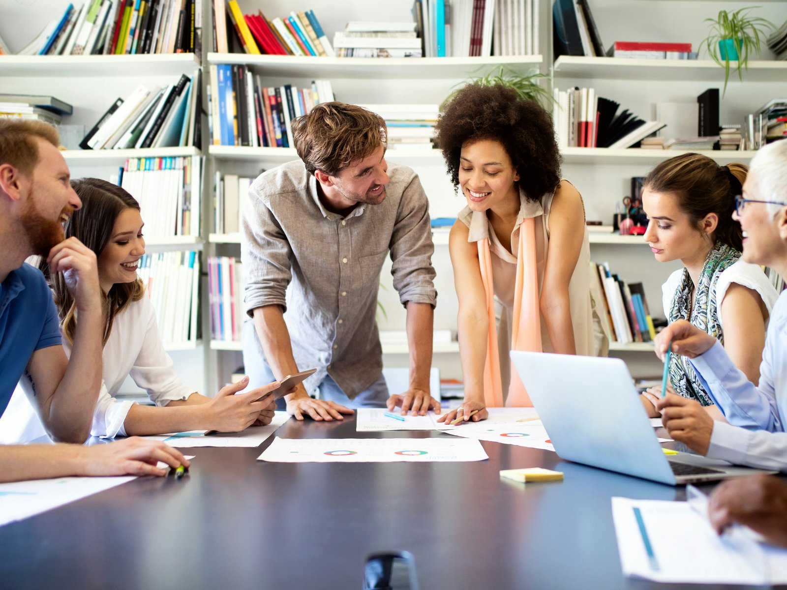 A hiring team gathered around a conference table with laptops and printed candidate notes, reviewing a role together